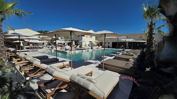 Ein Poolbereich mit Liegestühlen und Sonnenschirmen, ein klarer, blauer Himmel und ein Gebäude im Hintergrund.