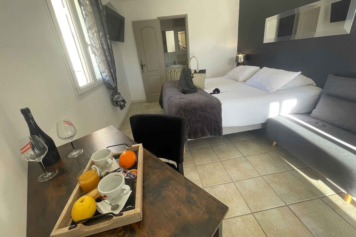 Une chambre d’hôtel comprenant un lit, un canapé, une table à manger avec un plateau de produits pour le petit-déjeuner, un téléviseur fixé au mur et une fenêtre avec des rideaux.