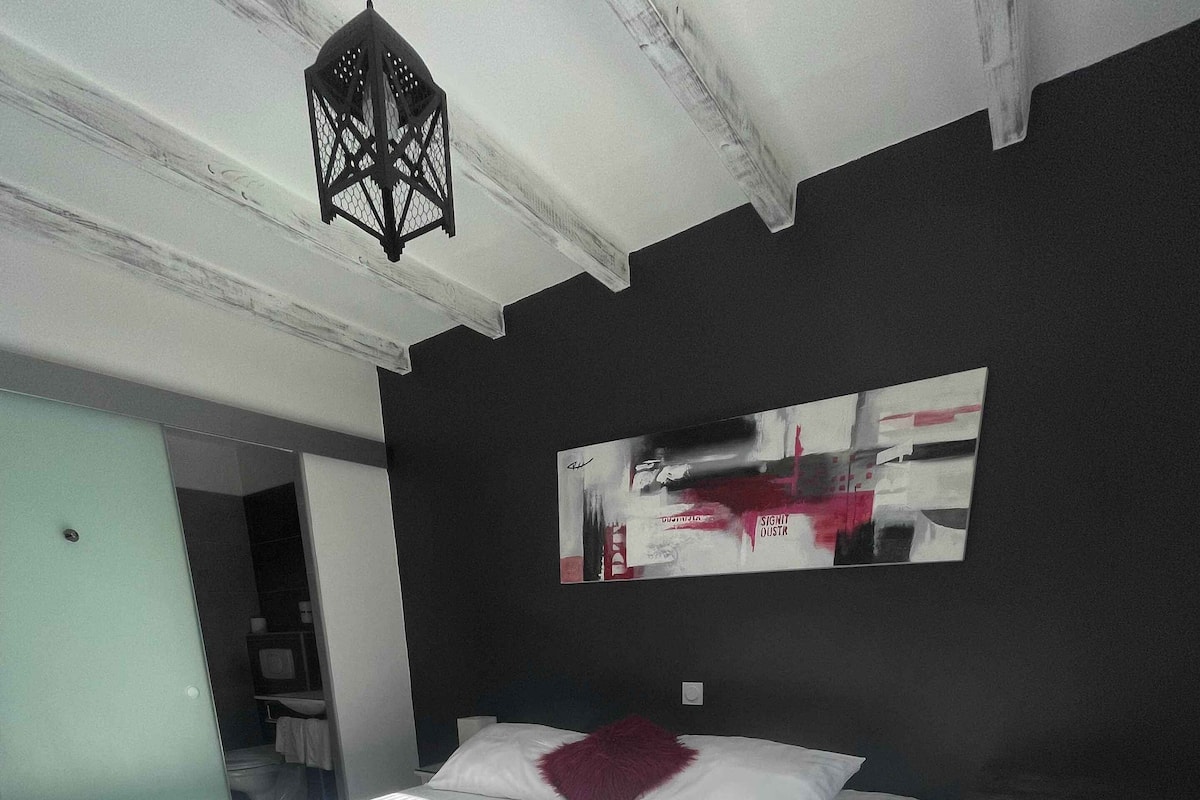 Une chambre moderne avec un grand lit, une table de chevet, un plaid rouge et un plateau contenant une tasse, une orange et un sac.