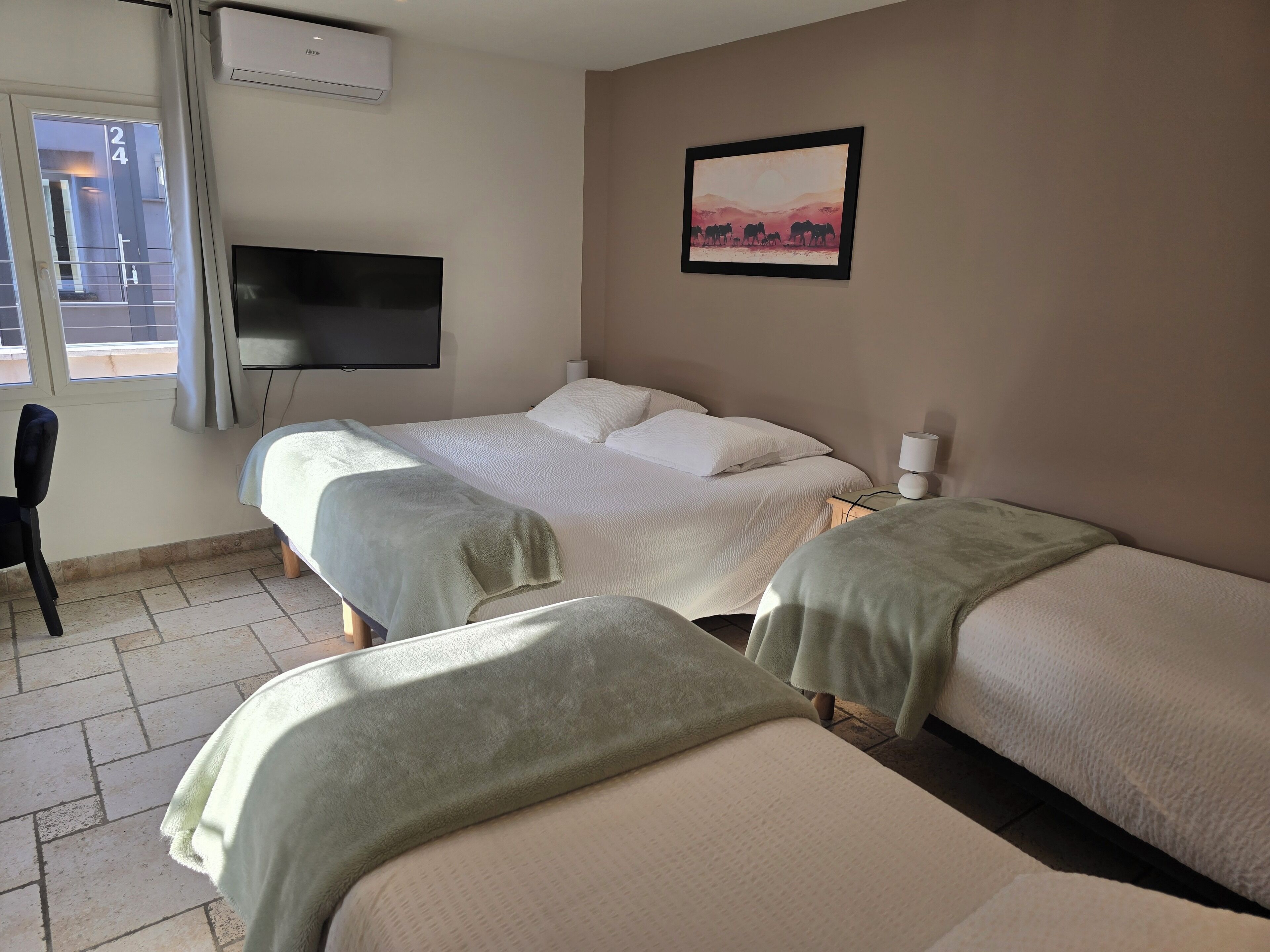 A hotel room with two beds, a TV, a painting, and a window.