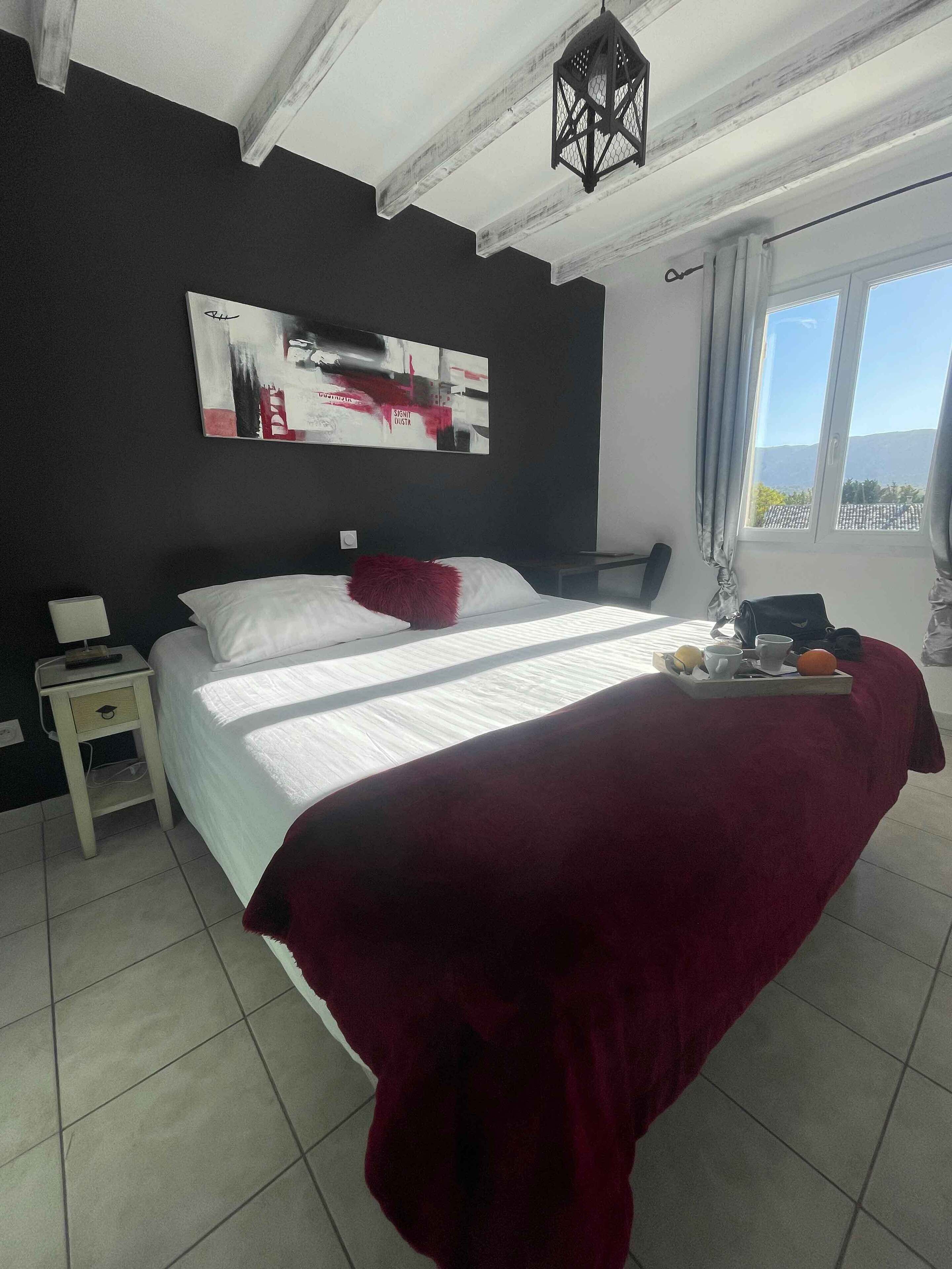 A bedroom with a large bed, a nightstand, a tray with breakfast items, and a view of the outdoors.