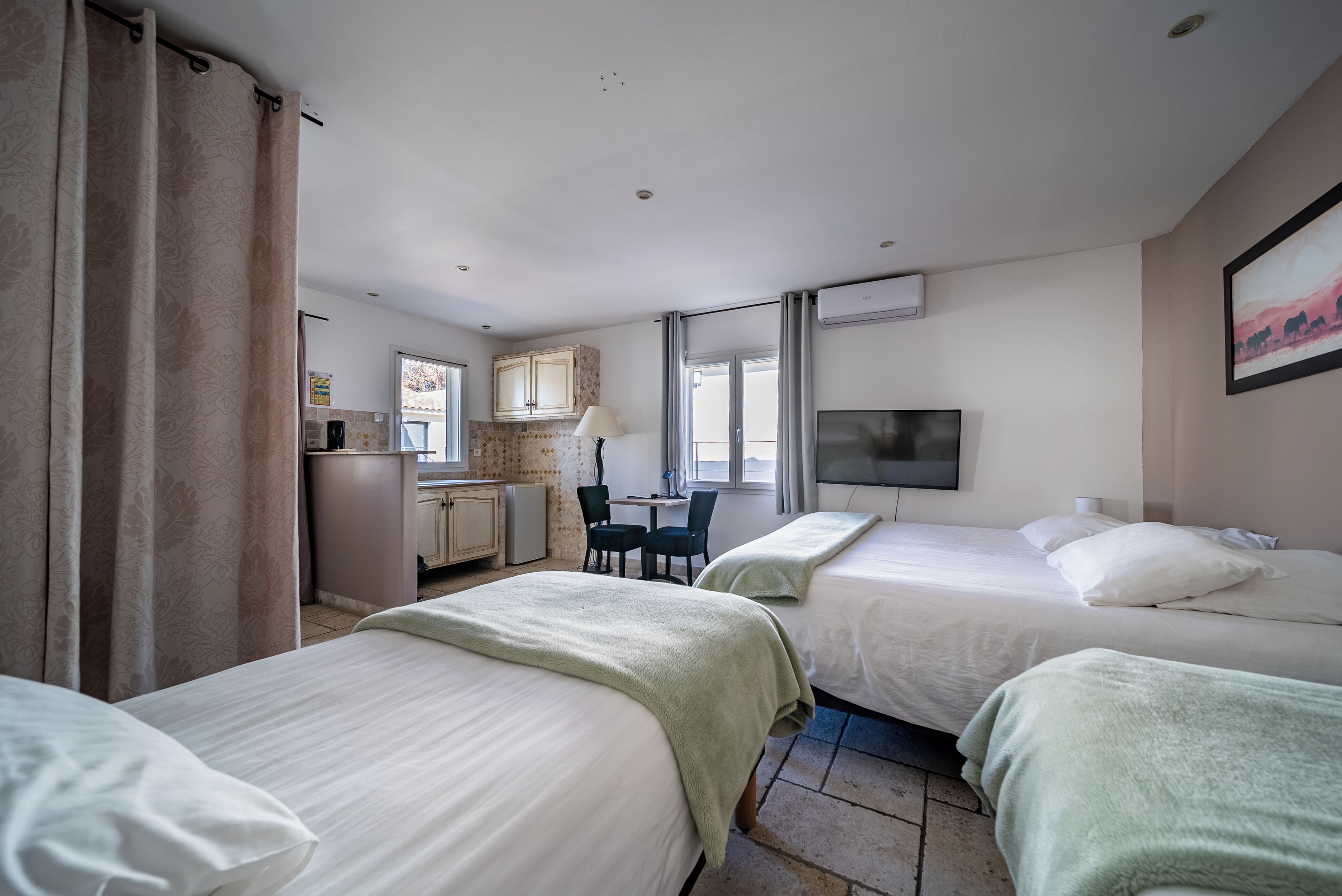 A hotel room with two beds, a desk with a chair, a TV, and a kitchenette.