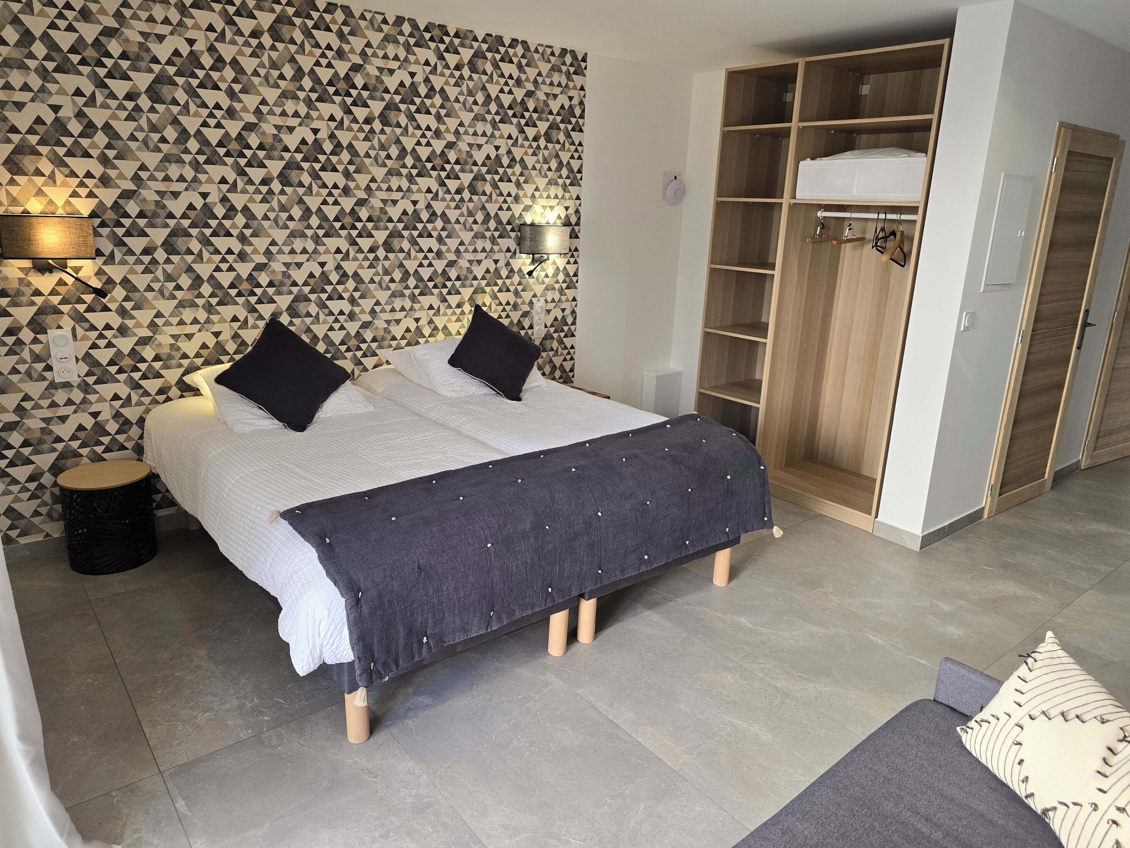 A bedroom with a bed, bedside lamps, a wardrobe, and a patterned wall.
