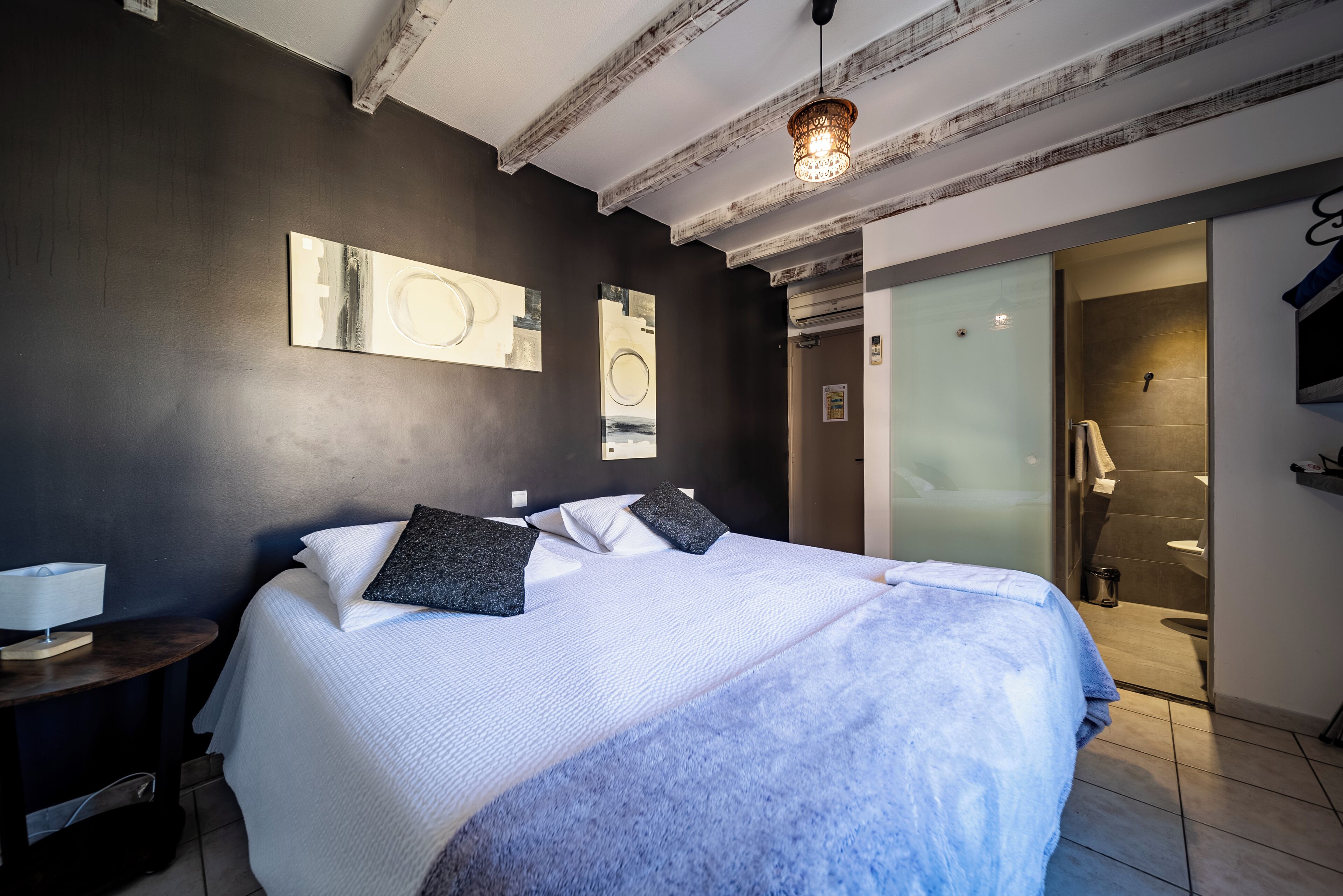 A modern hotel room with a large bed, a bedside table, and a glass shower enclosure.