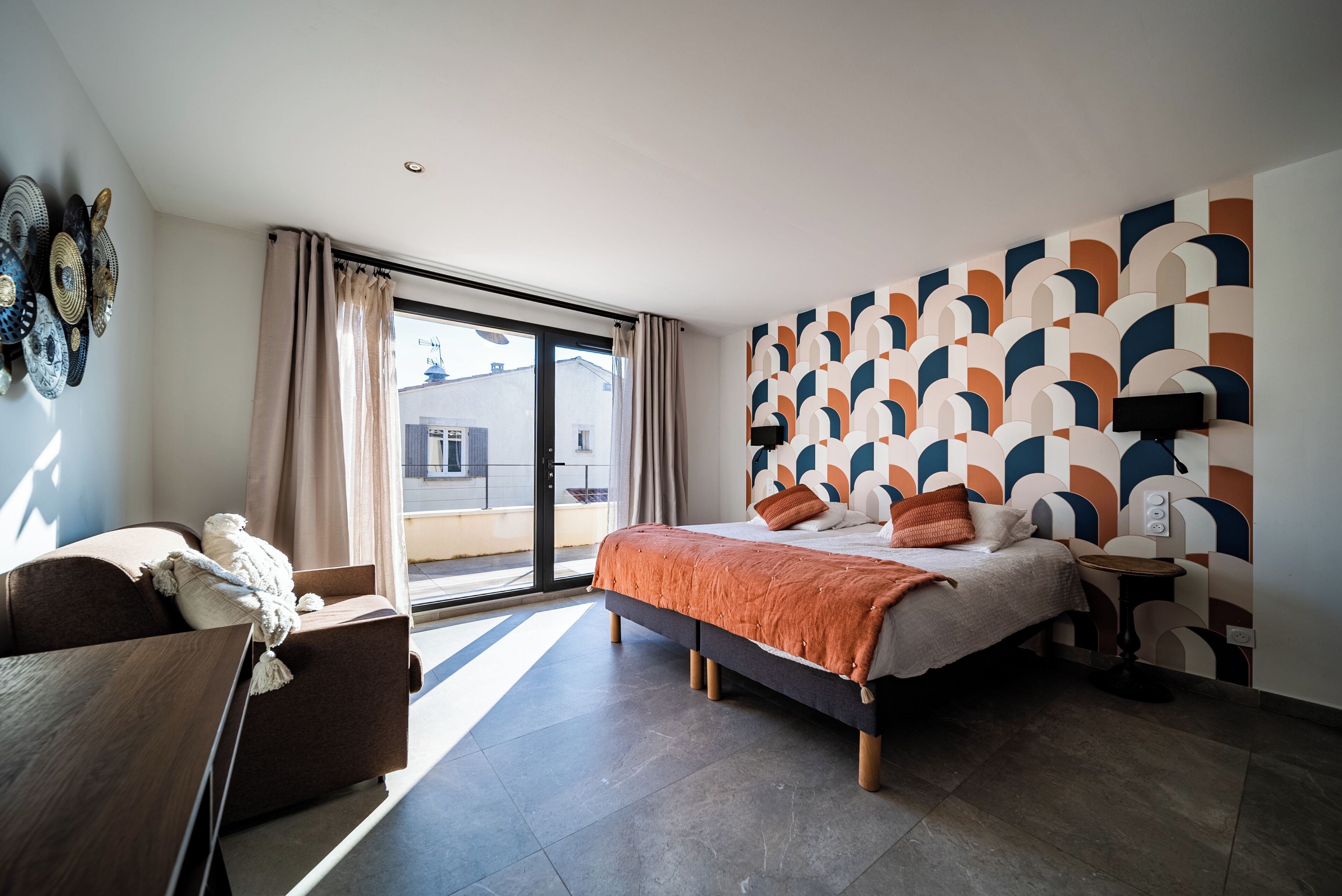 Quarto de hotel moderno com uma cama grande, um sofá, uma mesinha e vista para o exterior através de uma porta deslizante.