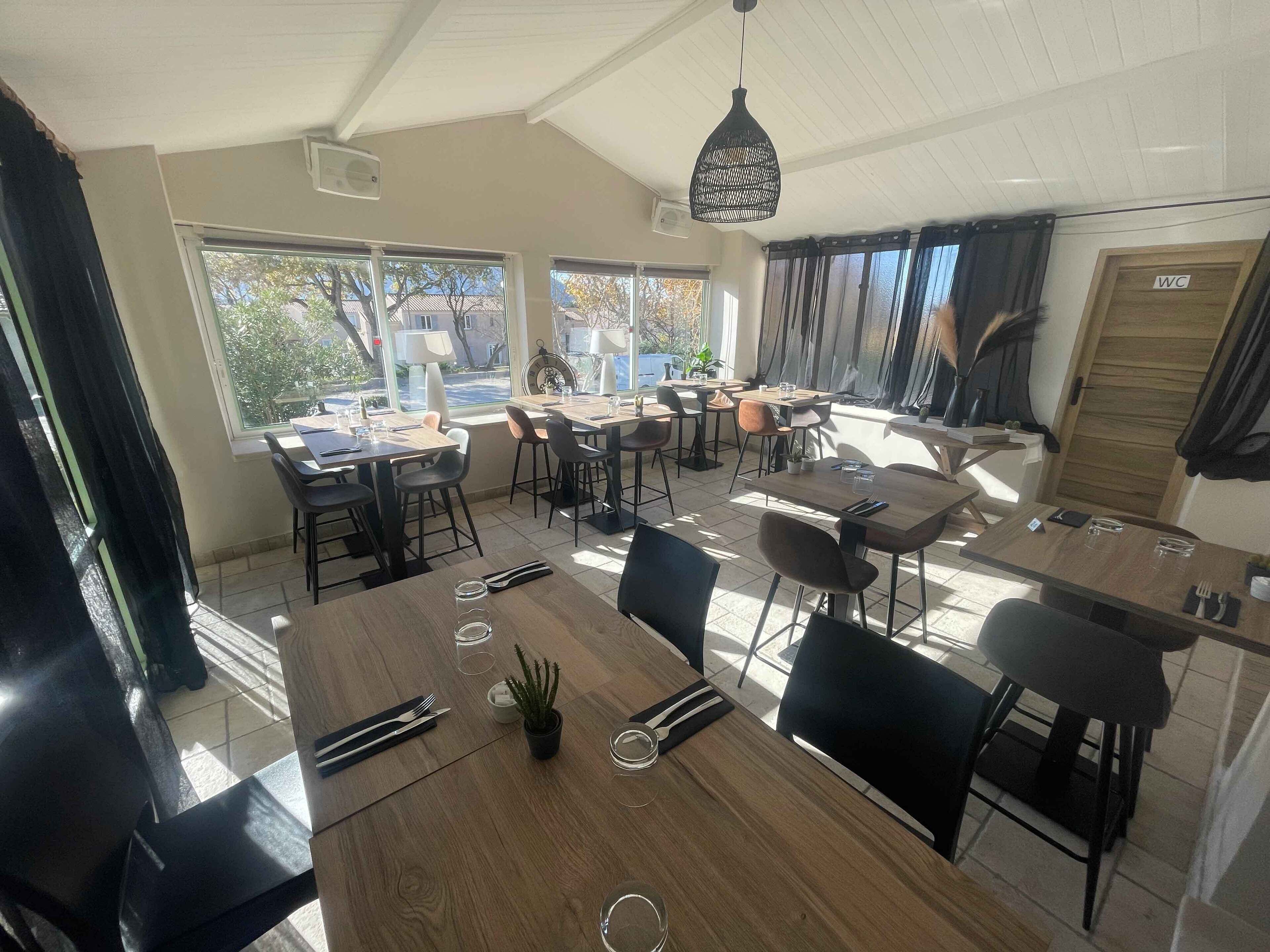 A dining area with multiple tables and chairs, large windows, and a ceiling fan.