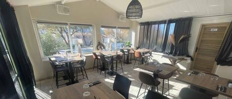 A dining area with multiple tables and chairs, large windows, and a ceiling fan.