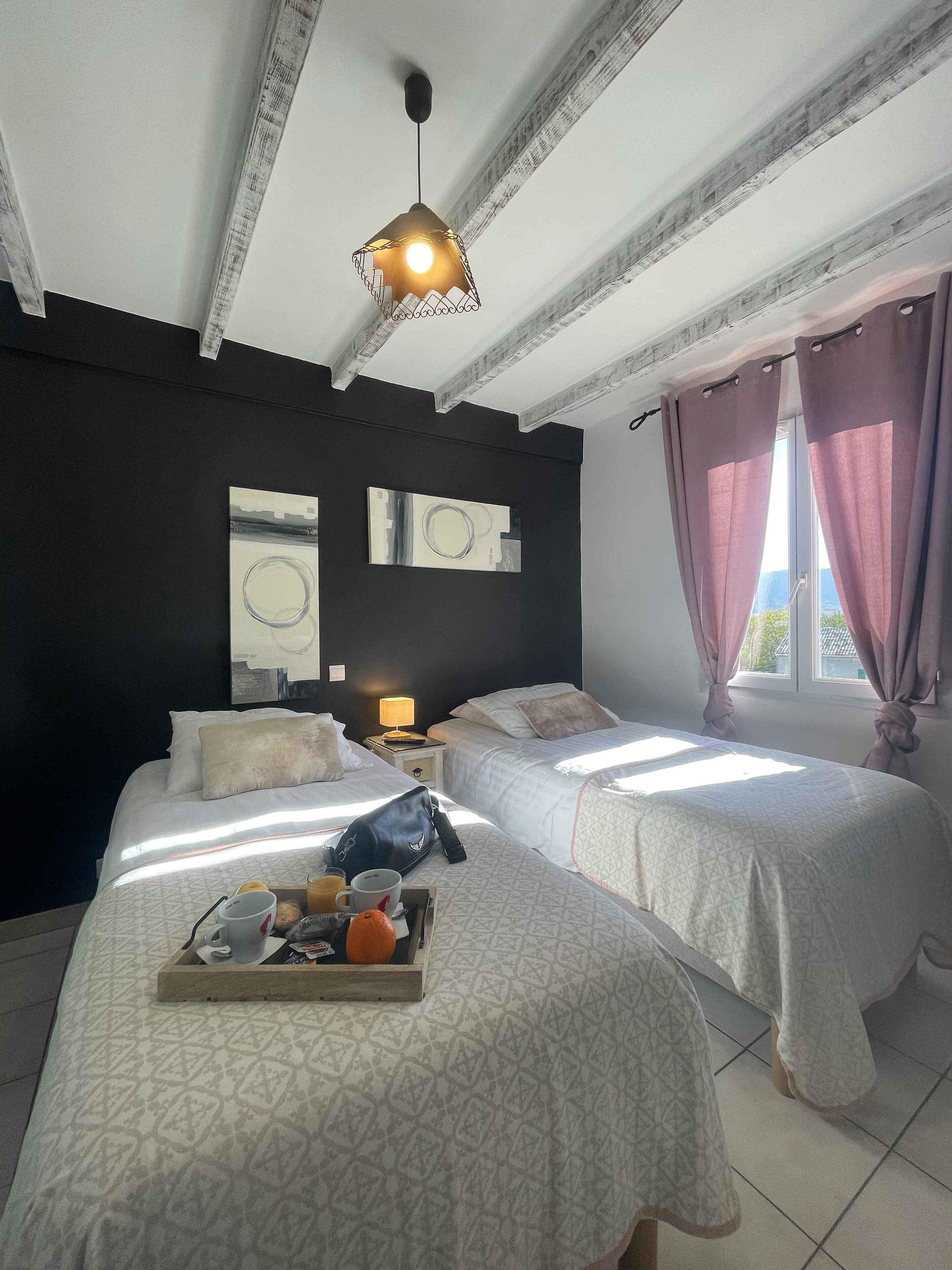 A hotel room with two beds, a ceiling light, a window with curtains, and a tray with breakfast items.