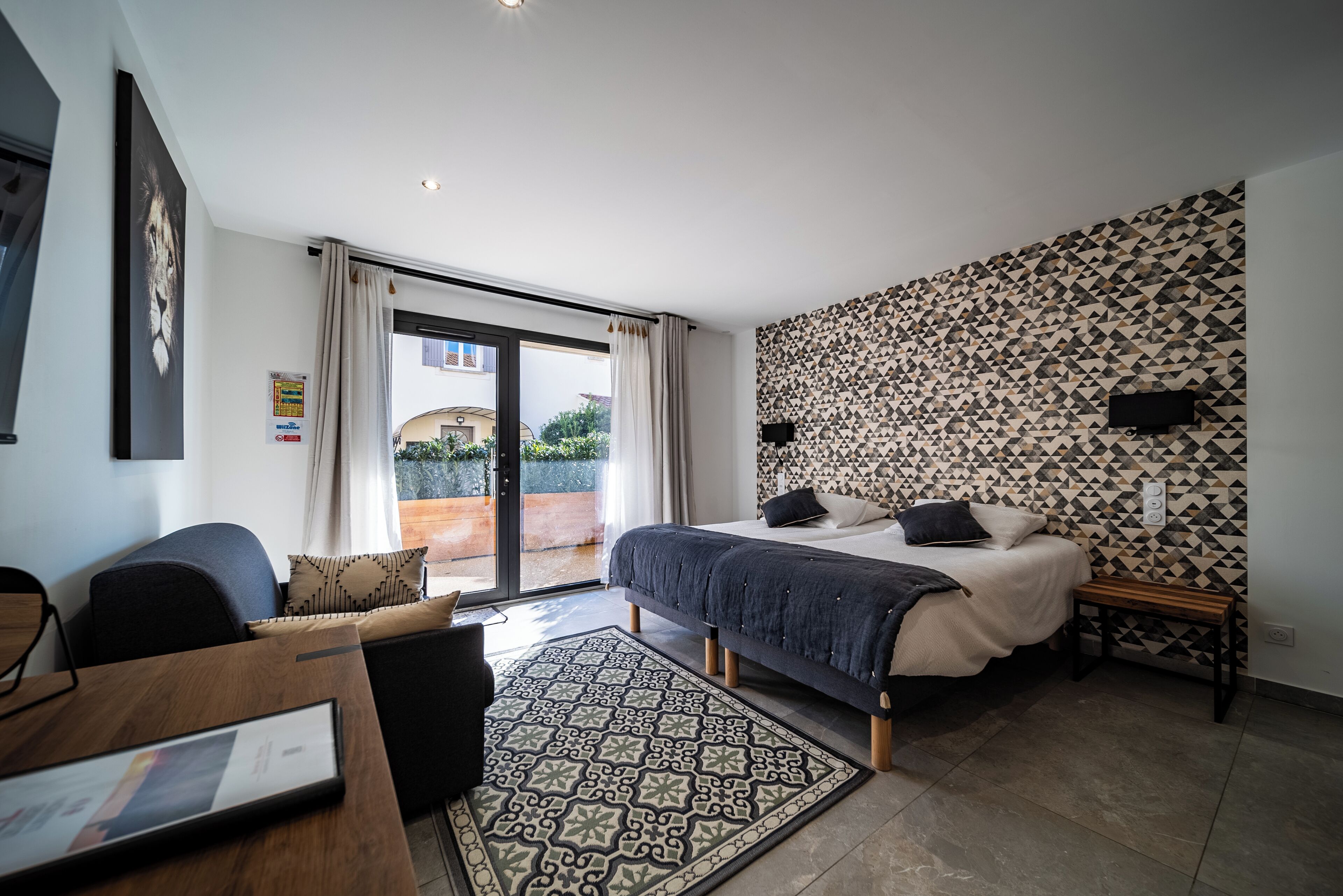 A modern bedroom with a large bed, a desk, and a view of the outdoors.