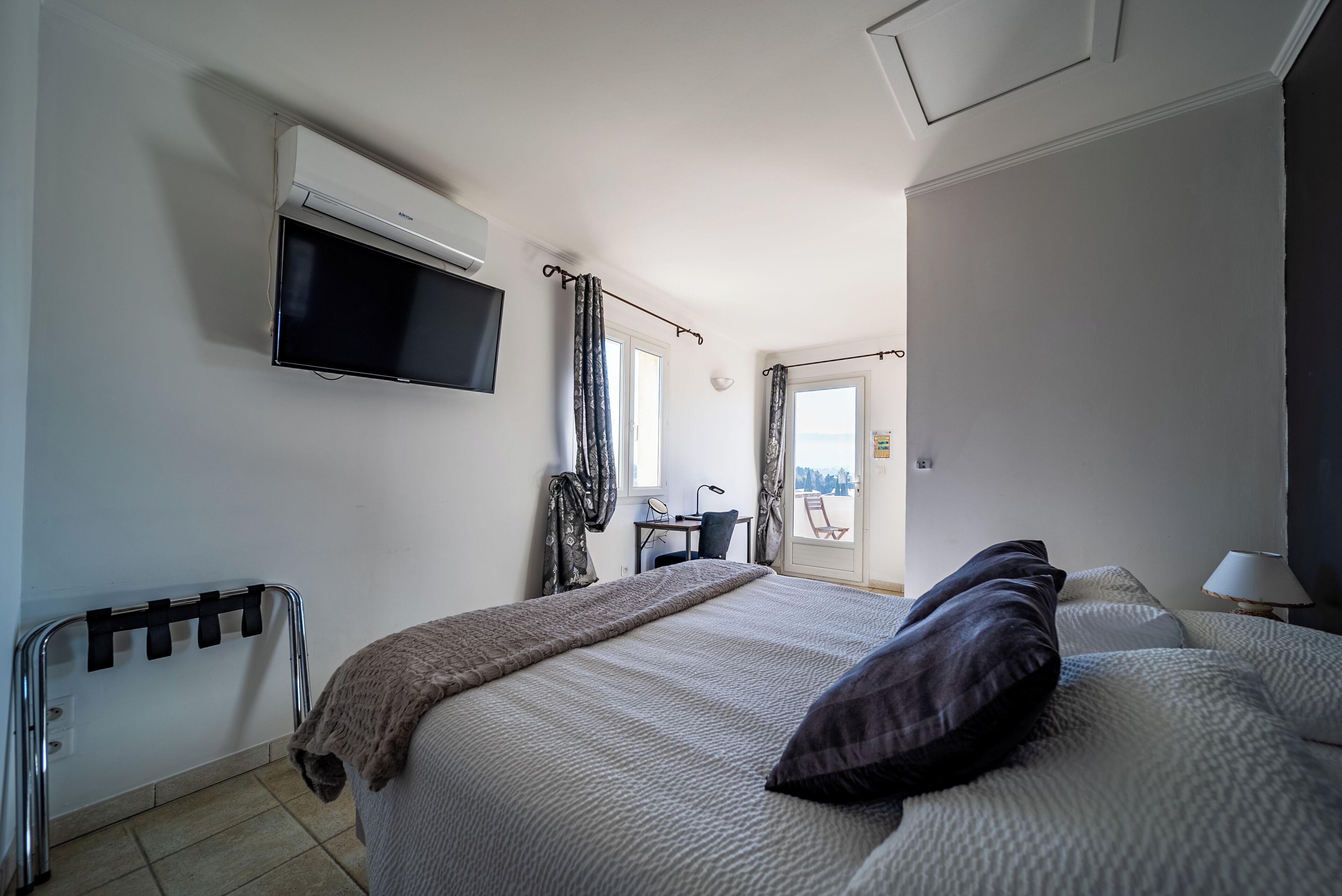 Une chambre d’hôtel avec un lit, un téléviseur fixé au mur, un bureau avec une chaise et une fenêtre avec des rideaux.