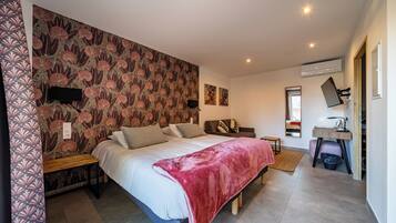 A bedroom with a large bed, a wooden bench, a red blanket, a wall-mounted TV, and a mirror.