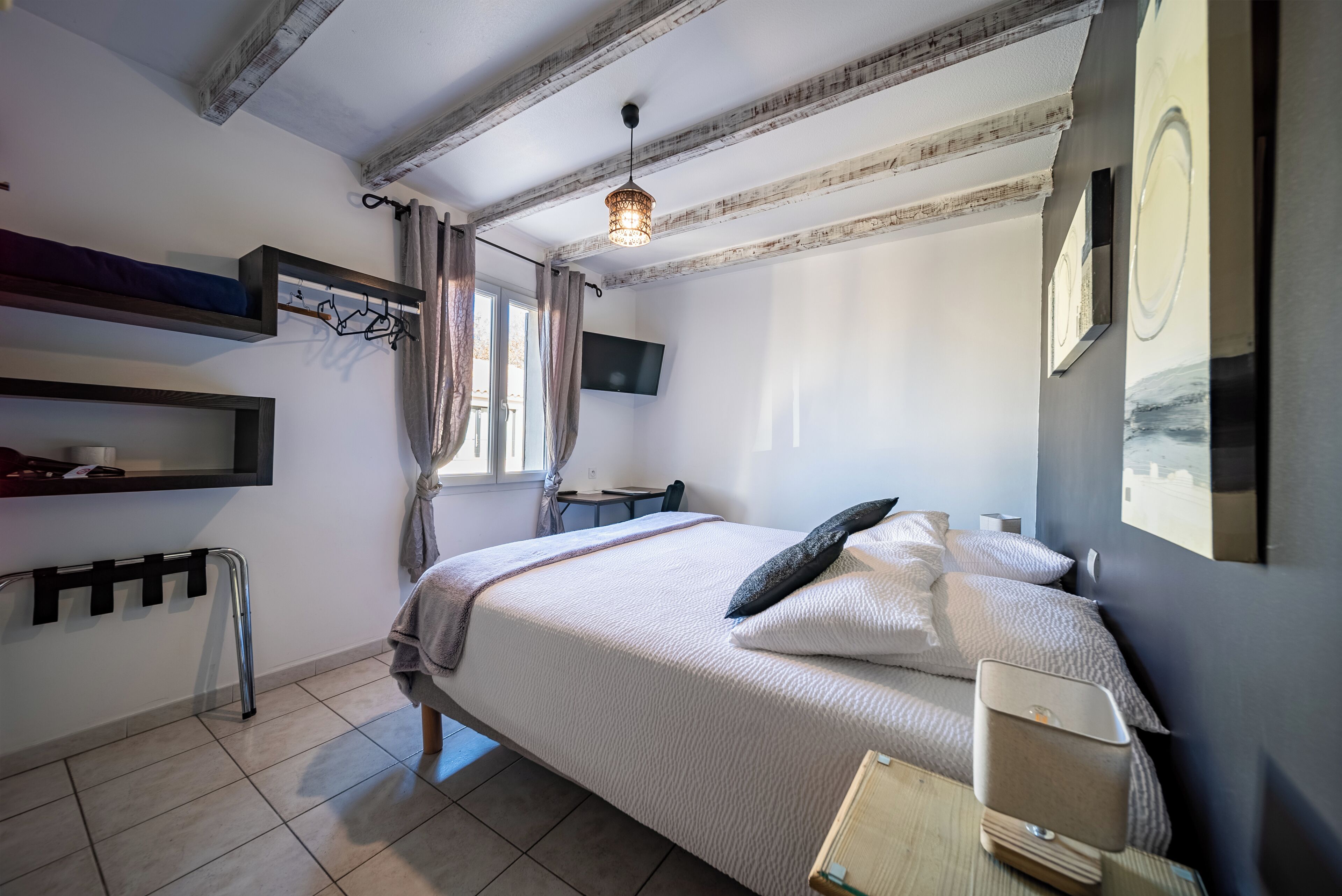 Een slaapkamer met een bed, nachtkastje, televisie en een raam met gordijnen.