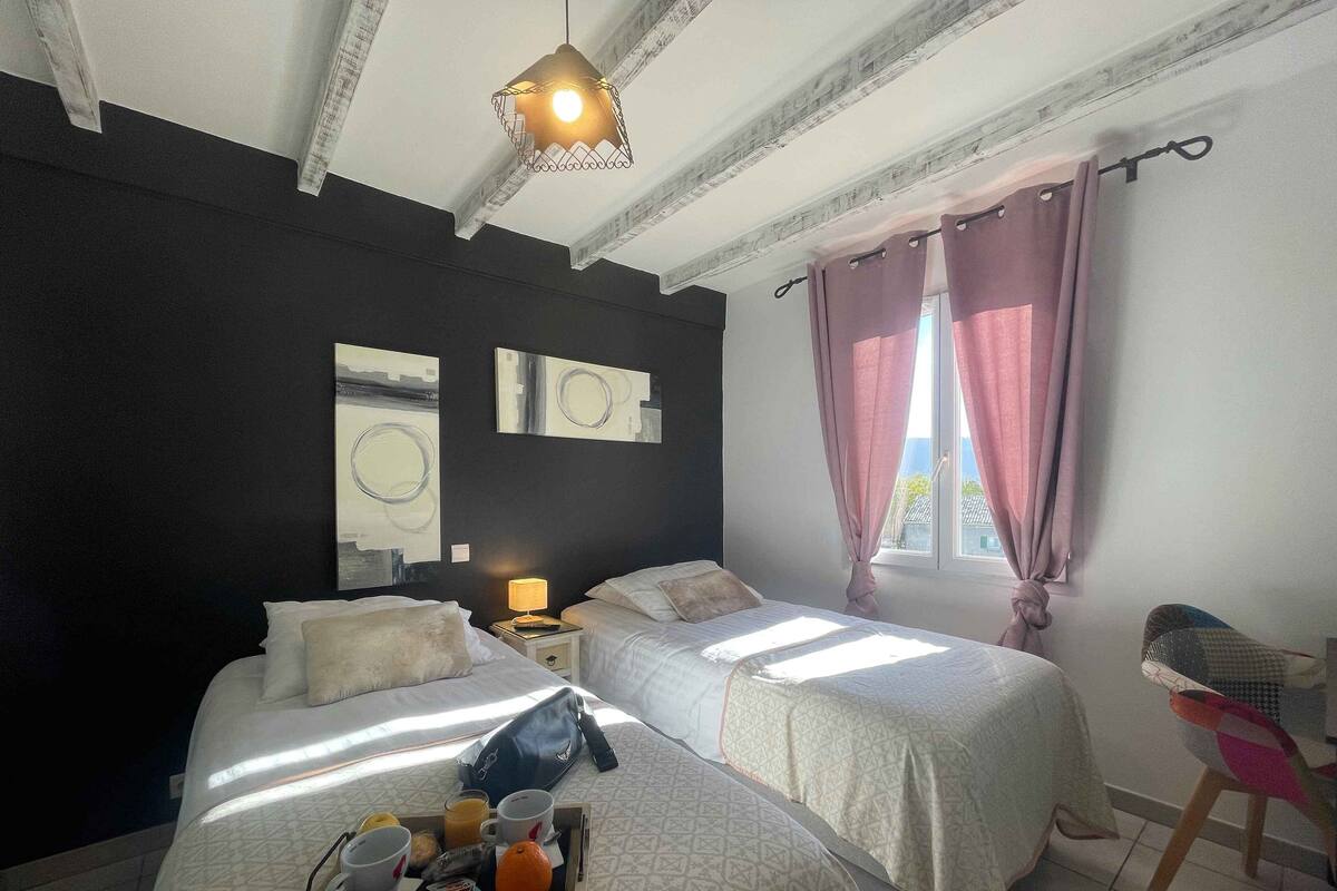 Une chambre d’hôtel avec deux lits, une table de chevet avec une lampe, un plateau avec des articles pour le petit-déjeuner et des œuvres d’art accrochées au mur.