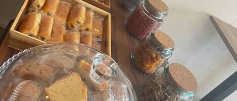 Una mesa con diversos alimentos, entre ellos pasteles y frascos con nueces y frutas secas.