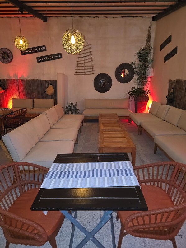 A cozy living area with a sectional sofa, a wooden coffee table, and wicker chairs. There are wall-mounted clocks and a decorative plant. - Les Loges du Luberon (Cabrieres-d'Avignon)