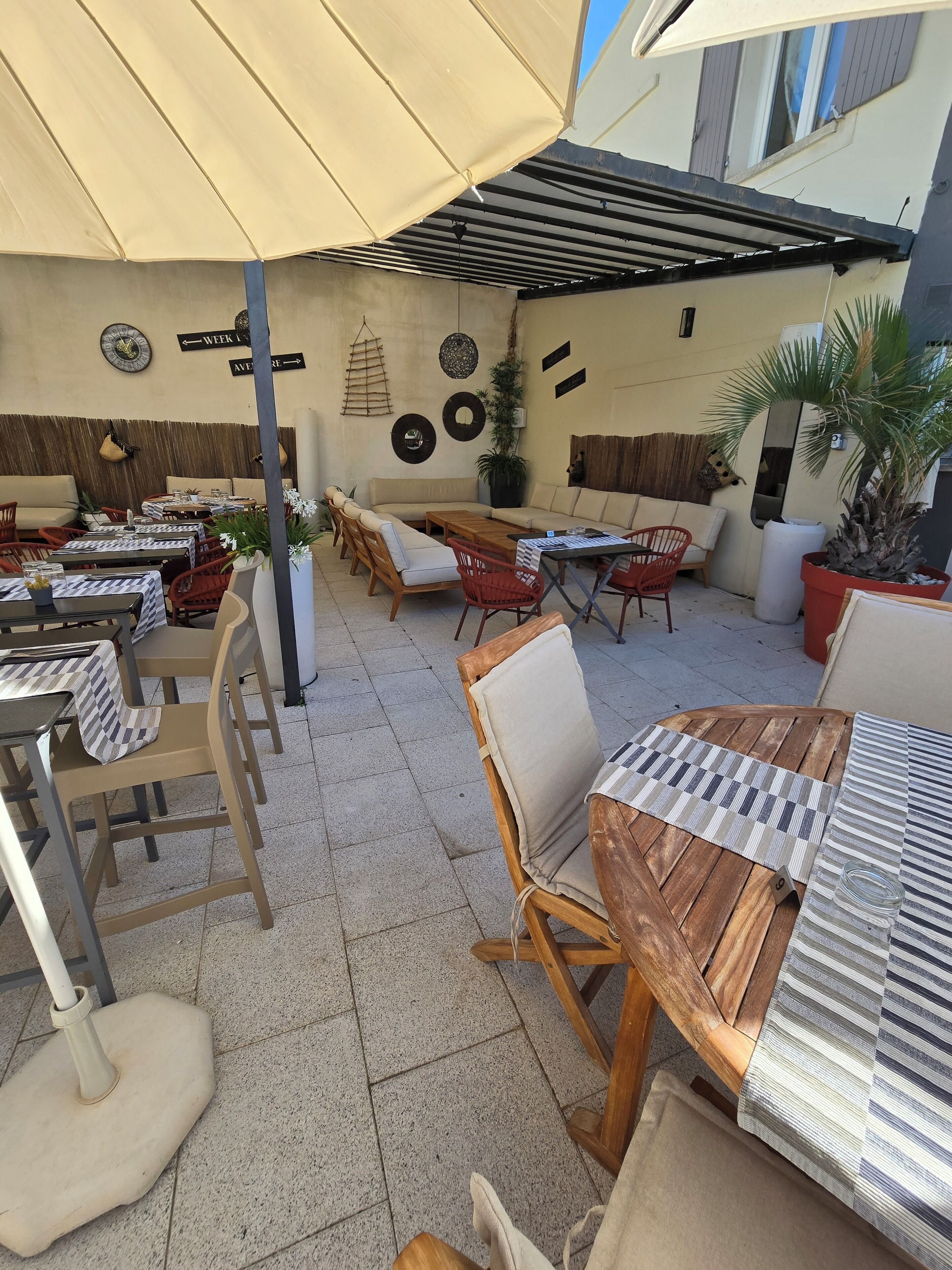 An outdoor patio area with tables and chairs, a wooden bench, and a large umbrella providing shade.