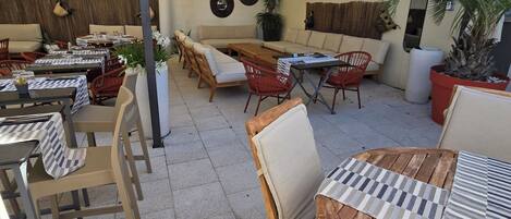 An outdoor patio area with tables and chairs, a wooden bench, and a large umbrella providing shade.