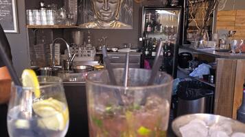 A bar area with a Buddha statue, a clock, and a variety of bottles and glasses.