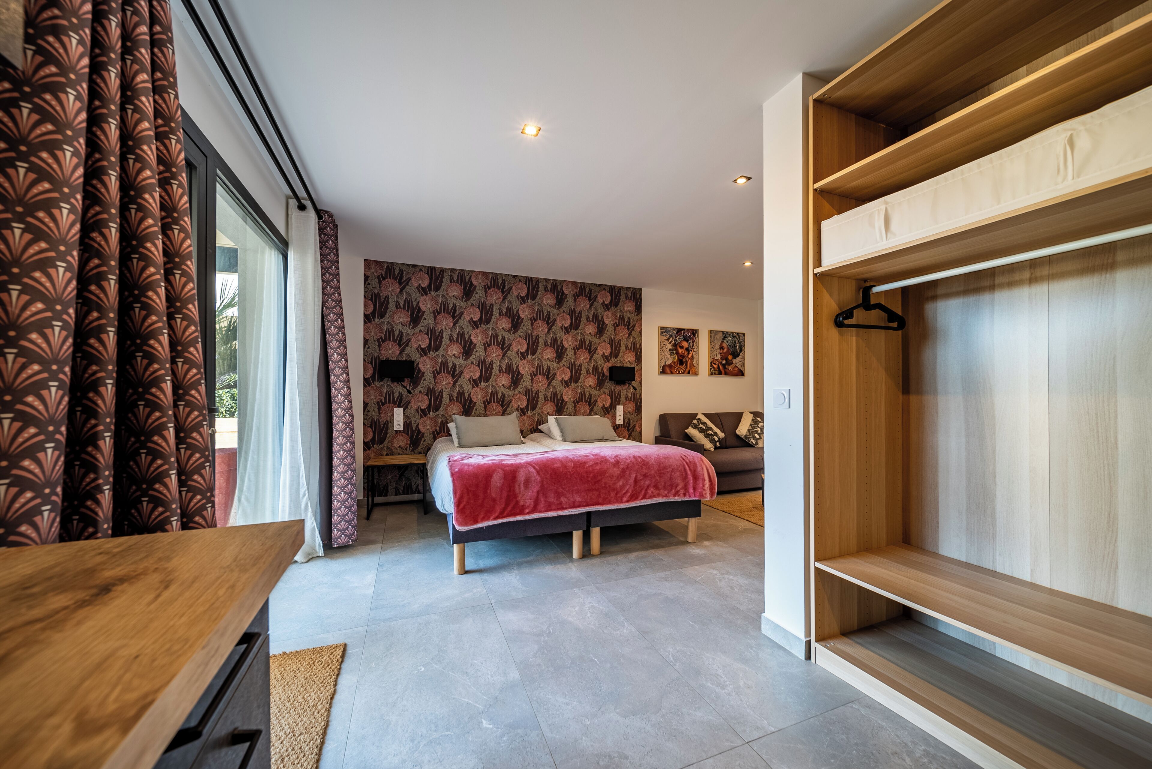 A modern bedroom with a bed, a wooden wardrobe, and a large window with patterned curtains.