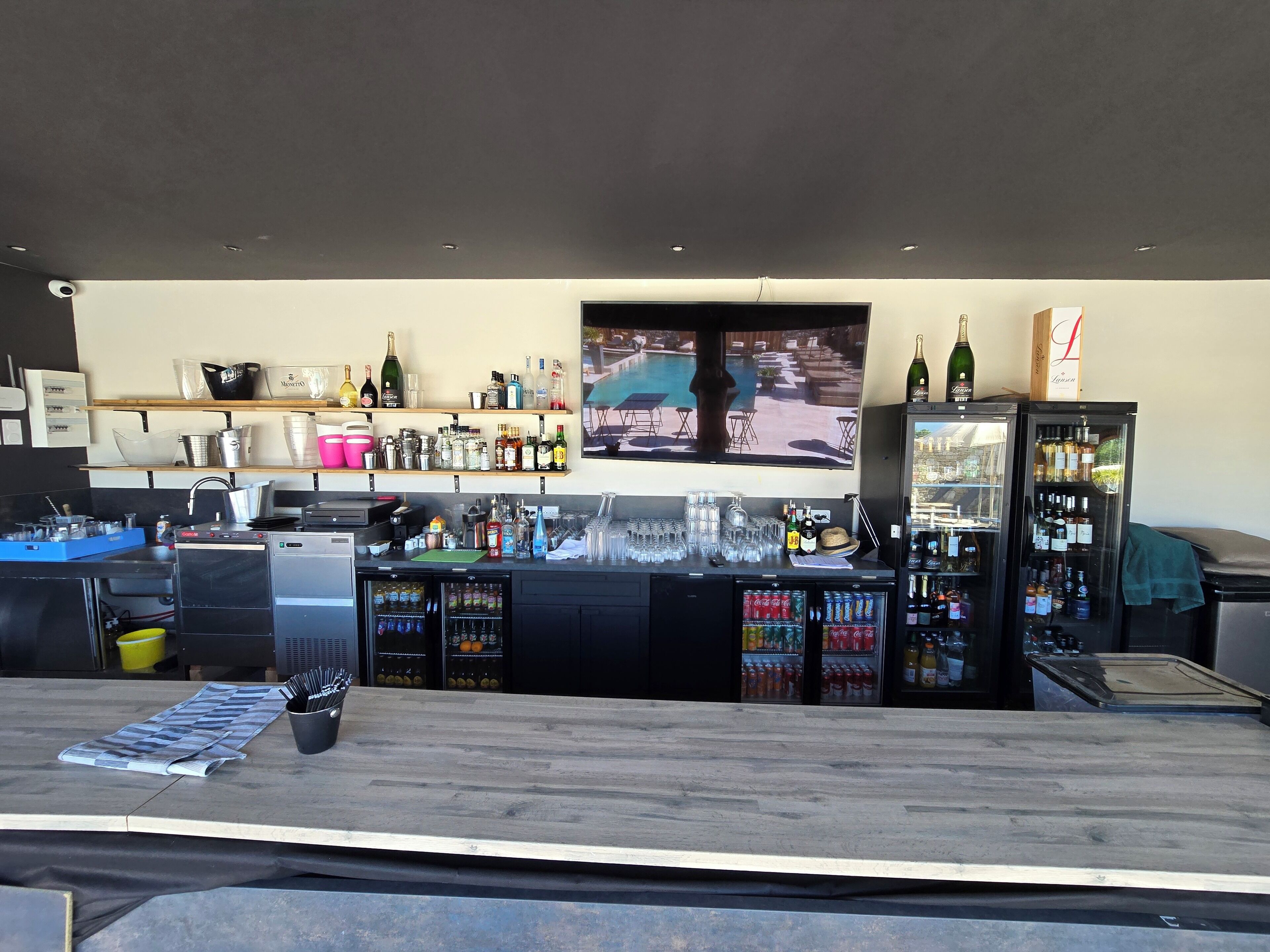 A bar area with a television screen, shelves with bottles, and a refrigerator.