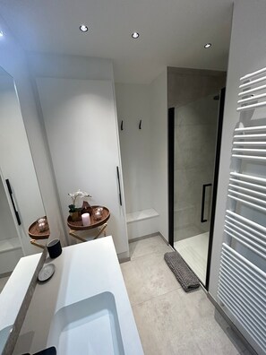 A modern bathroom with a white vanity, a glass shower enclosure, and a towel rack. - Appartement Chic et Confortable (Liege)