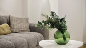 A green vase with foliage on a white round table in a living room with a grey sofa and a yellow pillow. - Appartement Chic et Confortable (Liege)