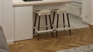 A modern kitchen with white cabinetry, a black microwave, and a wooden countertop. There are two white stools under the counter. - Appartement Chic et Confortable (Liege)