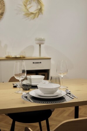 A dining table set with white plates, bowls, and wine glasses, with a placemat underneath. - Appartement Chic et Confortable (Liege)