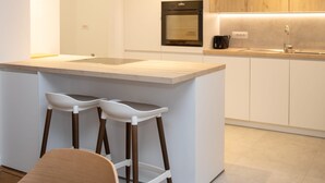 A modern kitchen with a central island, bar stools, a built-in oven, and a sink. - Appartement Chic et Confortable (Liege)