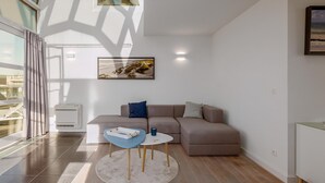 A modern living room with a sectional sofa, a small round table, and a large window with curtains.