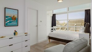 A bedroom with a bed, a dresser, a window with curtains, a chair, and a small table.