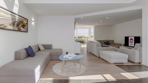 A modern living room with a sofa, ottoman, and a coffee table. There is a TV and a framed picture on the wall.