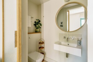 A bathroom with a toilet, a sink with a mirror, and a shelf with a plant. - Mason & Fifth, Bermondsey (London)