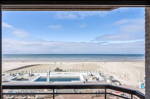 Blick auf einen Strand vom Balkon aus, mit Pool und Rettungsschwimmturm.
