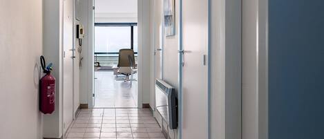 A hallway with a fire extinguisher, a radiator, and a chair in the distance.