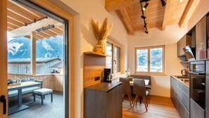 A modern kitchen with a wooden ceiling, a dining area with a bench, and a view of mountains through large windows. - Moiklerhof Apartment (Ramsau im Zillertal)