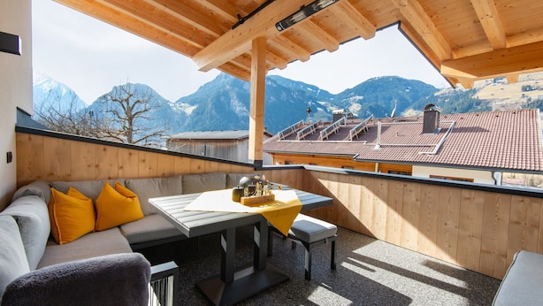 A wooden balcony with a table and seating, overlooking a mountainous landscape. - Moiklerhof Apartment (Ramsau im Zillertal)