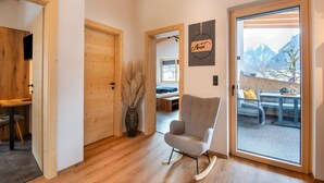 A modern interior with wooden floors, a rocking chair, a wooden door, and a view of mountains through a glass door. - Moiklerhof Apartment (Ramsau im Zillertal)