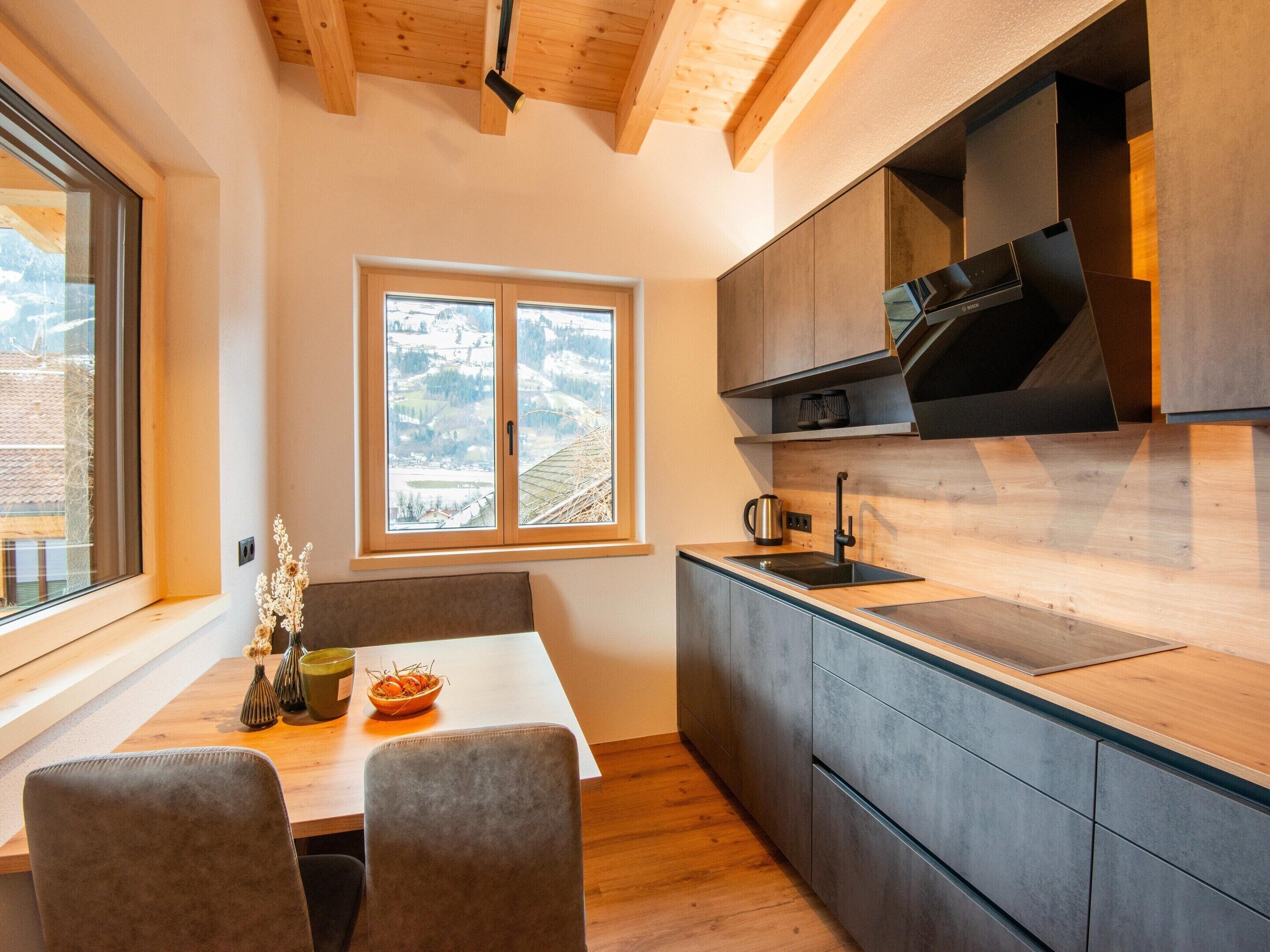 A modern kitchen with wooden cabinets, a black stove, and a window with a view of a snowy landscape.