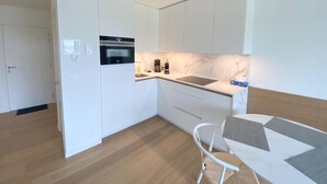 A modern kitchen with white cabinetry, a built-in oven, a sink, and a dining area with a white chair and table. - 1 bedroom accommodation in Nieuwpoort (Nieuwpoort)