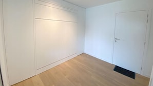 A room with a wooden floor, white walls, and a door. - 1 bedroom accommodation in Nieuwpoort (Nieuwpoort)