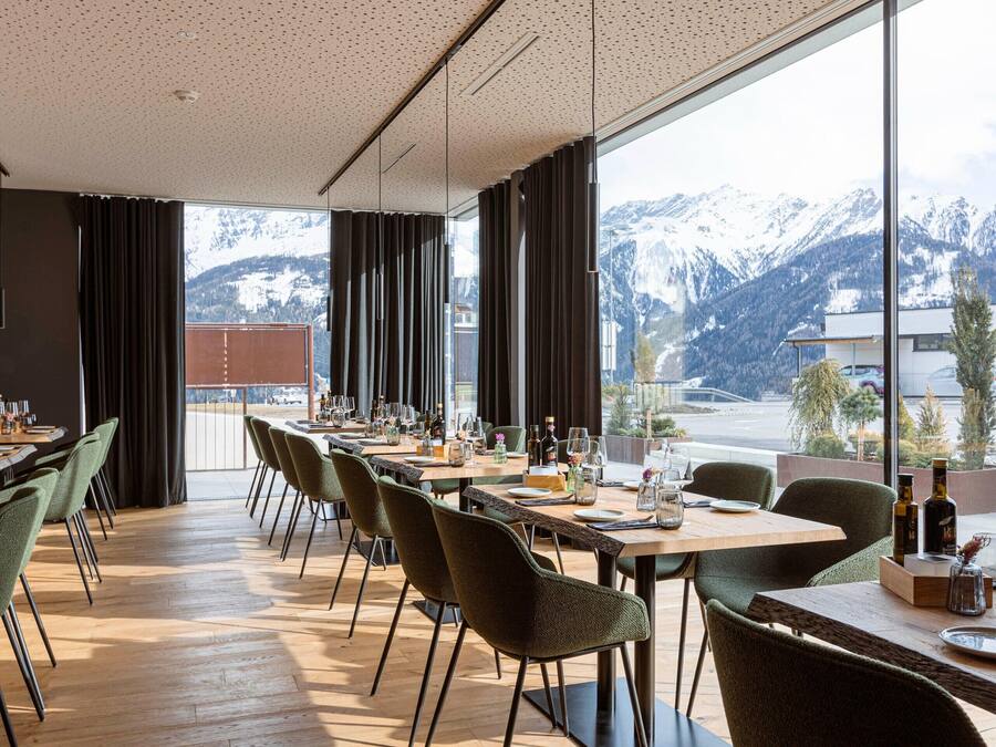 A dining area with tables set for a meal, large windows with a mountain view, and a modern interior design.