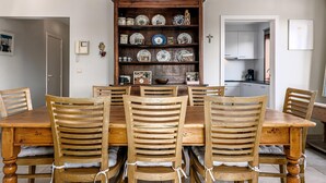 A dining room with a wooden table and chairs, a china cabinet with dishes, and a kitchen in the background.