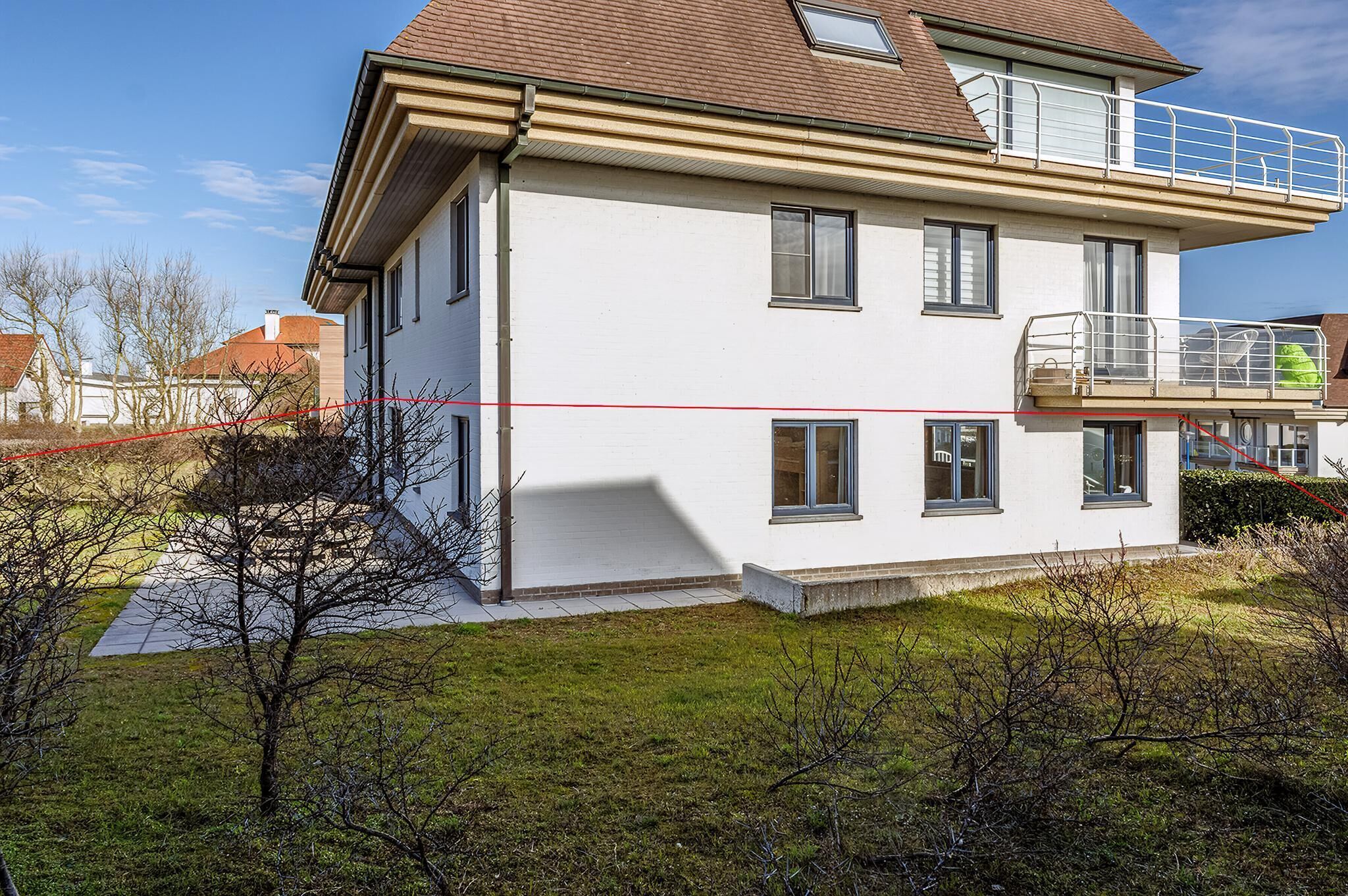 Een huis met twee verdiepingen, een balkon, een zichtbaar raam en een kleine tuin.