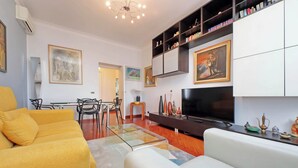 A living room with a yellow sofa, a white sofa, a glass coffee table, a TV, and shelves with decorative items. - Una finestra sulla cupola di San Pietro (Rome)