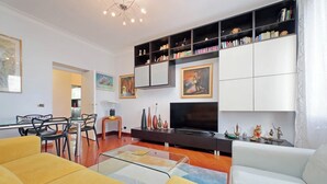 A modern living room with a sofa, a coffee table, a TV, a bookshelf, and a dining area with chairs and a table. - Una finestra sulla cupola di San Pietro (Rome)