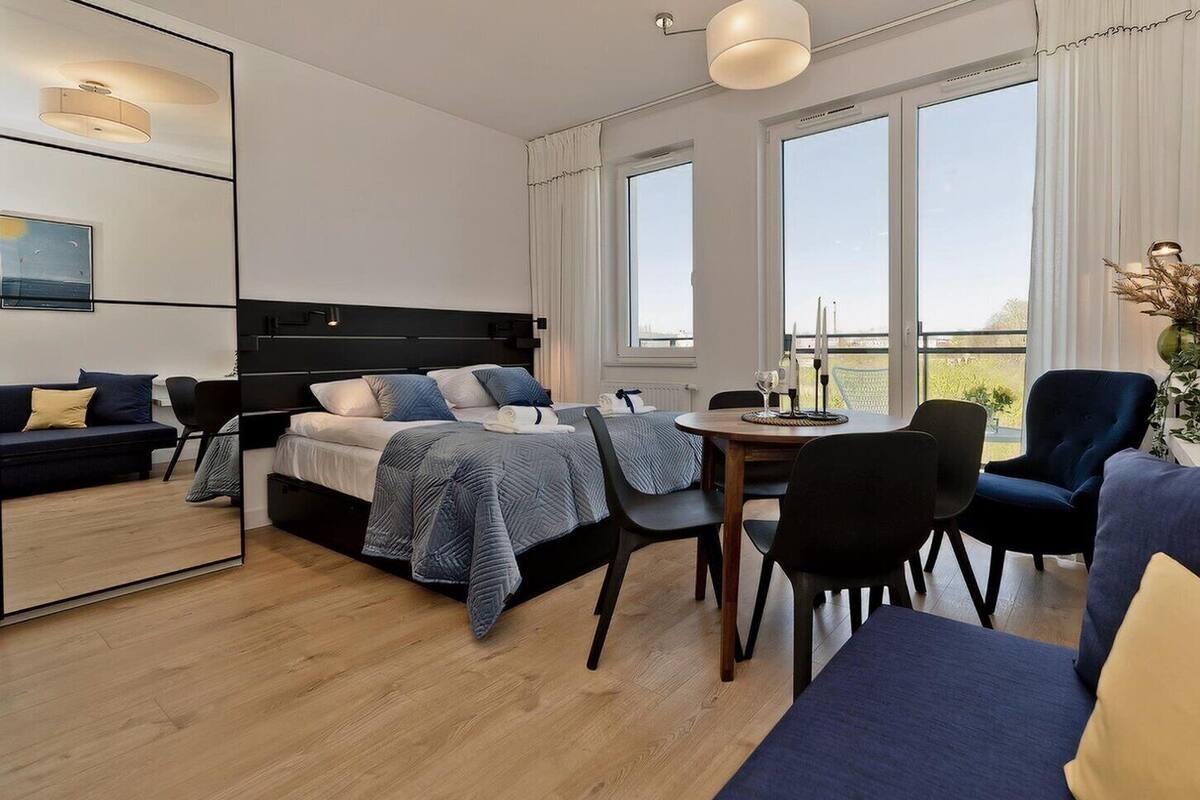 Une chambre d’hôtel moderne, dotée d’un grand lit, d’une table à manger et d’un canapé. De grandes fenêtres laissent entrer la lumière naturelle et offrent une vue sur l’extérieur.