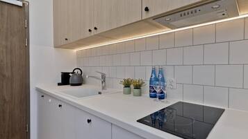 Una cocina moderna con armarios blancos, una placa de inducción negra, una tetera y dos plantas en macetas.