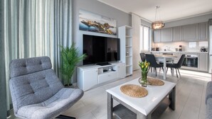 A modern living room with a grey sofa, a flat-screen TV, and a dining area with a table and chairs. - Apartamenty NEXO - Puck by Q4Apartments  (Puck)