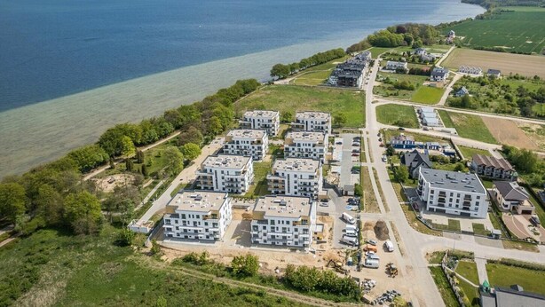 An aerial view of a coastal residential area with modern apartment buildings, a marina, and a clear view of the sea. - Apartamenty NEXO - Puck by Q4Apartments  (Puck)